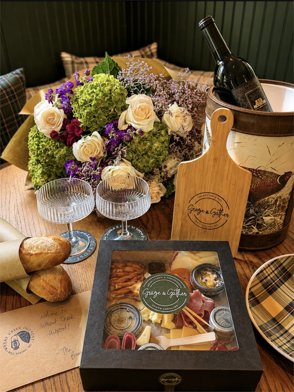 A Graze & Gather welcome box with a branded serving board, chilled wine, fresh flowers and a handwritten card set out for an arrival