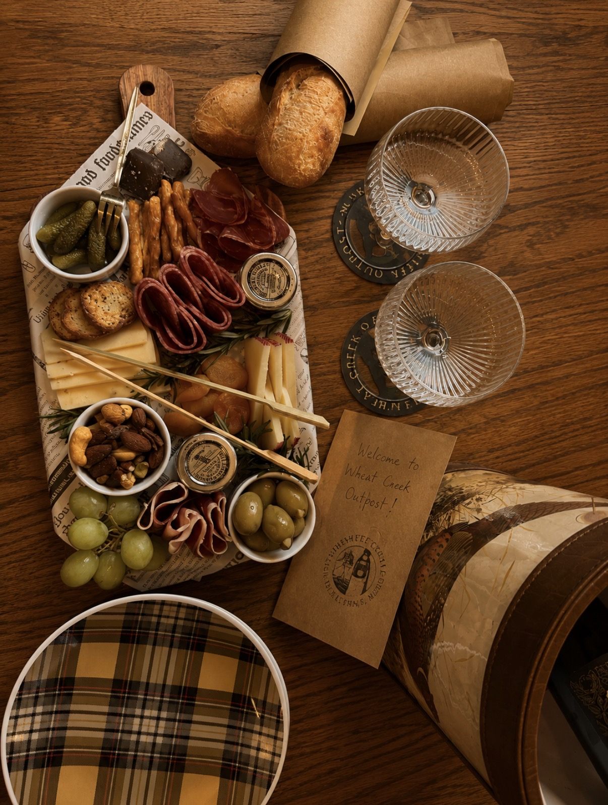 An overhead view of a Graze & Gather board with cured meats, cheeses, cornichons, nuts and grapes, served with bread, glassware and a handwritten welcome card