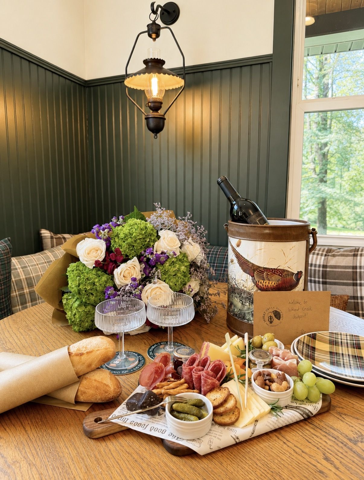 A styled Graze & Gather board with chilled wine, fresh flowers, glassware and a handwritten welcome card set on a tasting room table